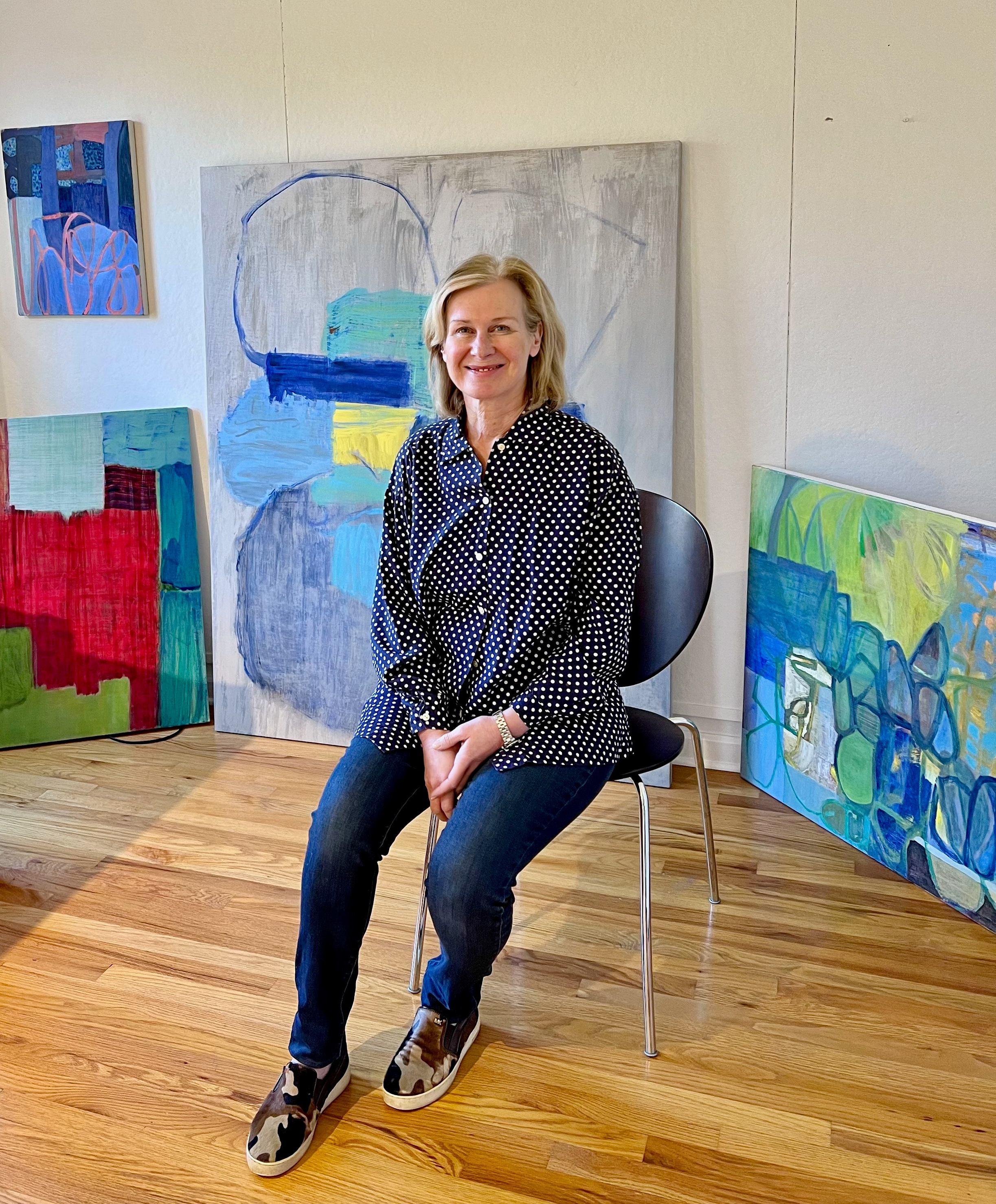 Donna Scarpa sitting in front of some of her paintings in her studio